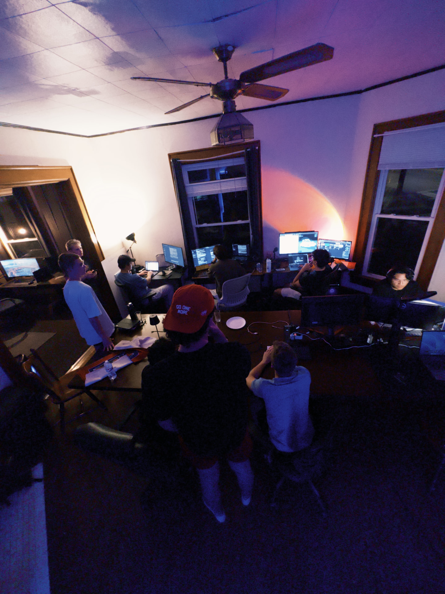 Hustle House fellows working late at night together on laptops and monitors in the house work room
